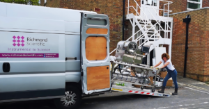 Woman pushing trolley with scientific equipment onto a grey van with 'Richmond Scientific' on the side