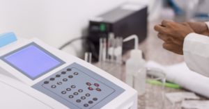 Photo of UV-vis spectrophotometer in a laboratory with various glassware in the background